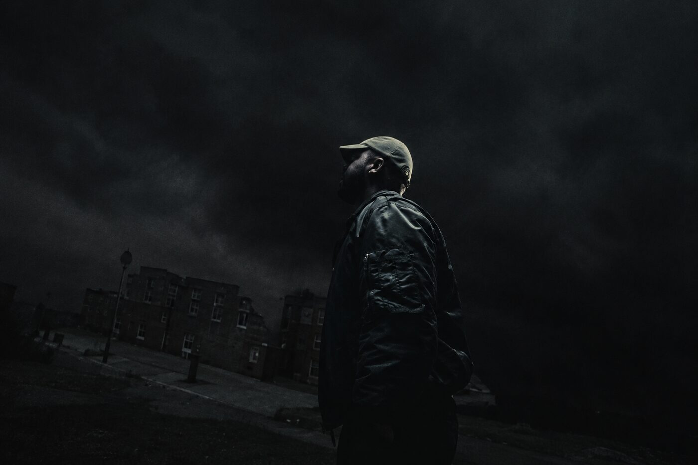 Silhouette of a man in a cap against a smoky night sky over a housing estate, still from Archy Moor “Robbery Rings”